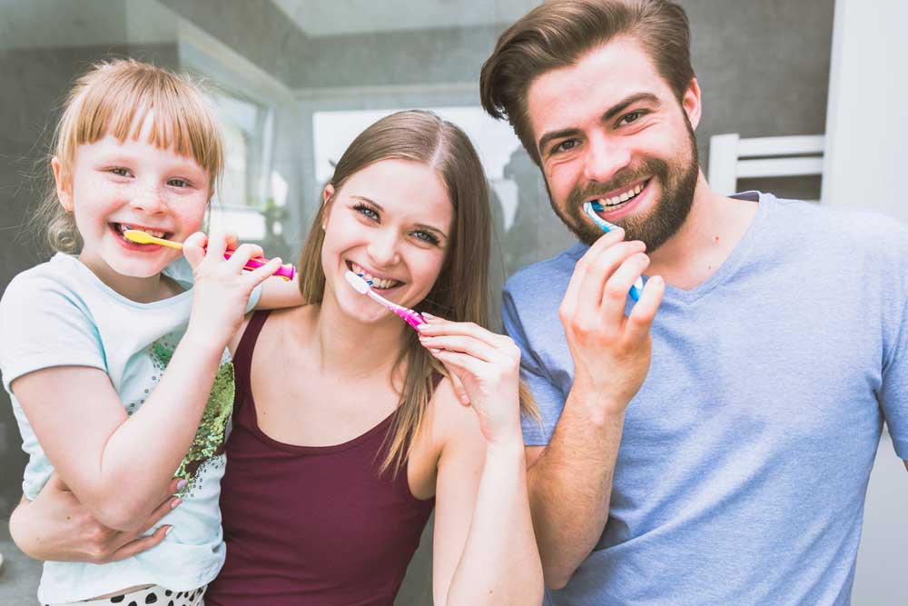 A family of three all smiling and brushing their teeth.
