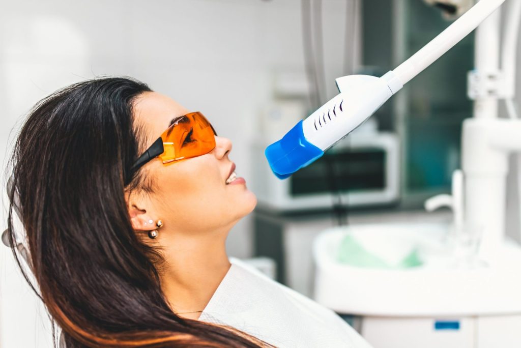 Woman in orange safety glasses having her teeth whitened