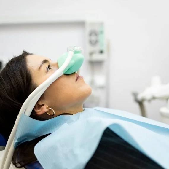 Patient tilts back in dental chair while dental professional applies nasal sedation mask